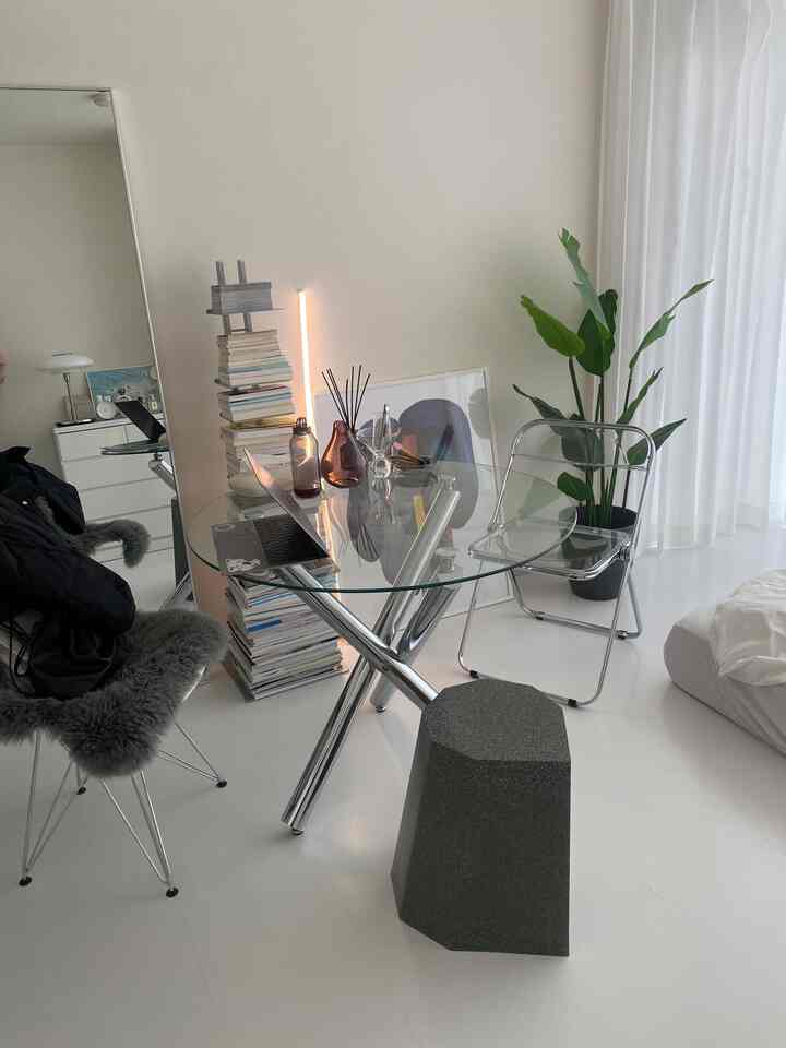 Bright white-toned home office with glass dining table, transparent chair, and green plant in a modern interior