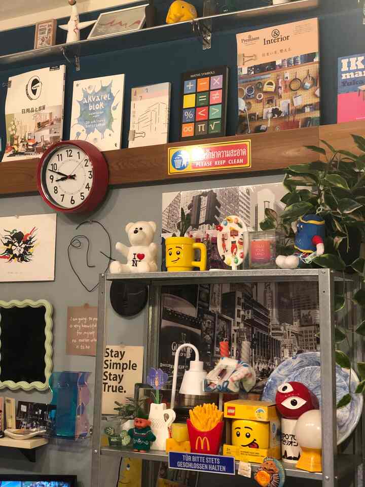 Dark-toned living room featuring metal shelves with various retro decor items and plants, wall clock and posters arranged for aesthetic interior