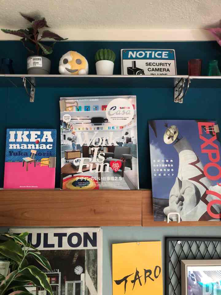 ディープブルーの壁にメタルシェルフと木製シェルフが配置されたリビングの飾り棚、様々な雑誌と小さなオブジェが雰囲気を演出