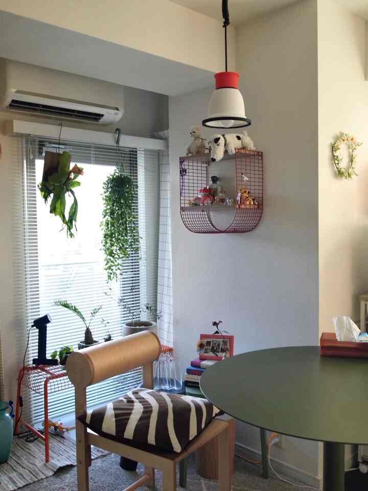 Beige-toned living room featuring plants, wood-tone dining chair, and green round table in cozy arrangement