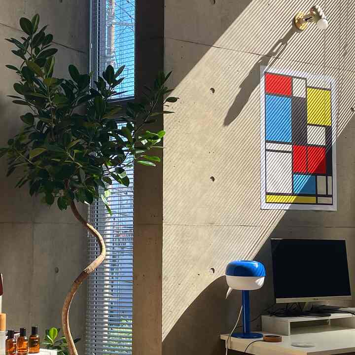 自然光が差し込むコンクリートの壁、ミッドセンチュリーモダンの壁アートと青いテーブルランプがあるモダンな空間