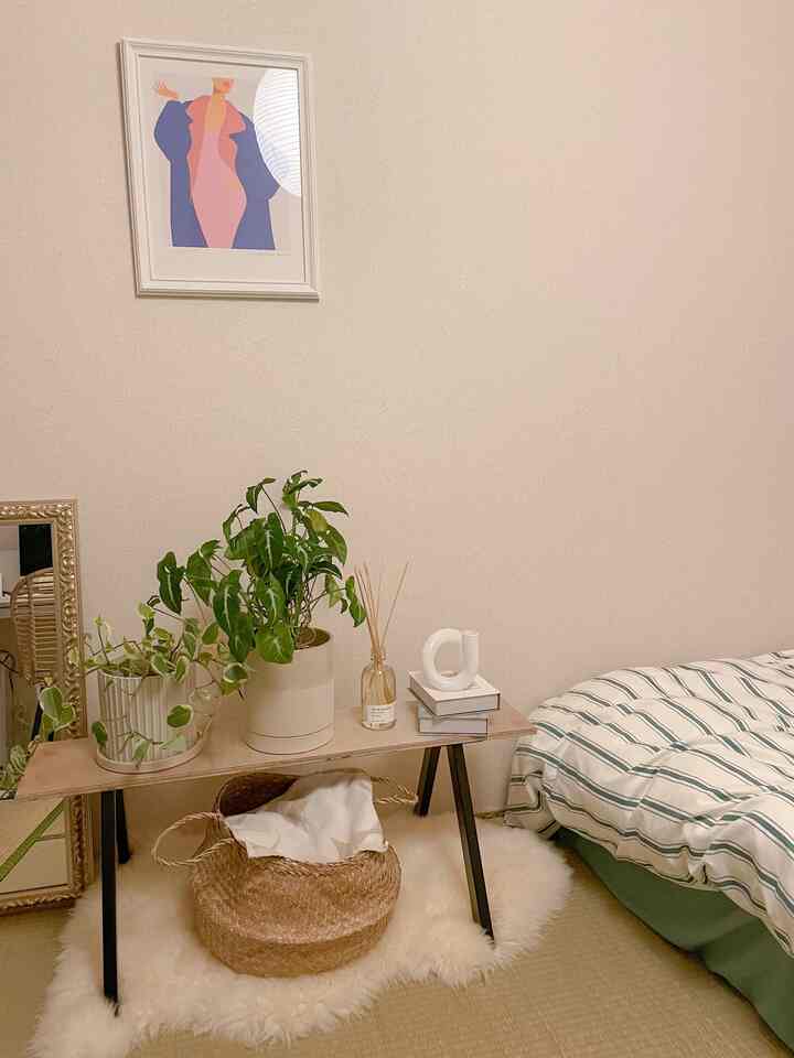 ナチュラルカラーの寝室、木製テーブルに植物とバスケット、ストライプのベッドカバーが配置された落ち着いた雰囲気のインテリア