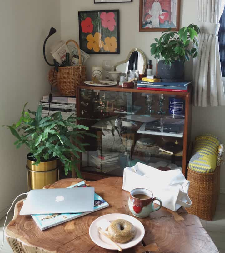 A white-walled natural living room featuring wood tone coffee table, glass cabinet, and green plants creating a cozy ambiance