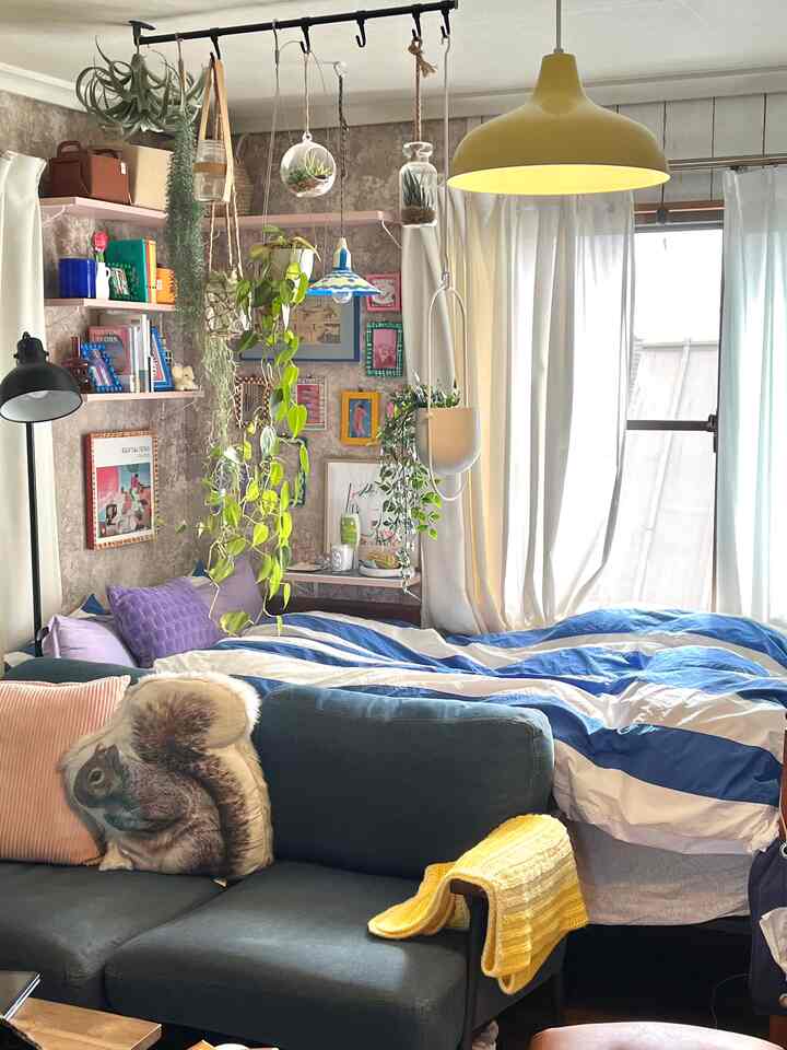 ナチュラルな色調の寝室、カラフルな額縁やペンダントライト、植物とソファが配置された雰囲気のある空間