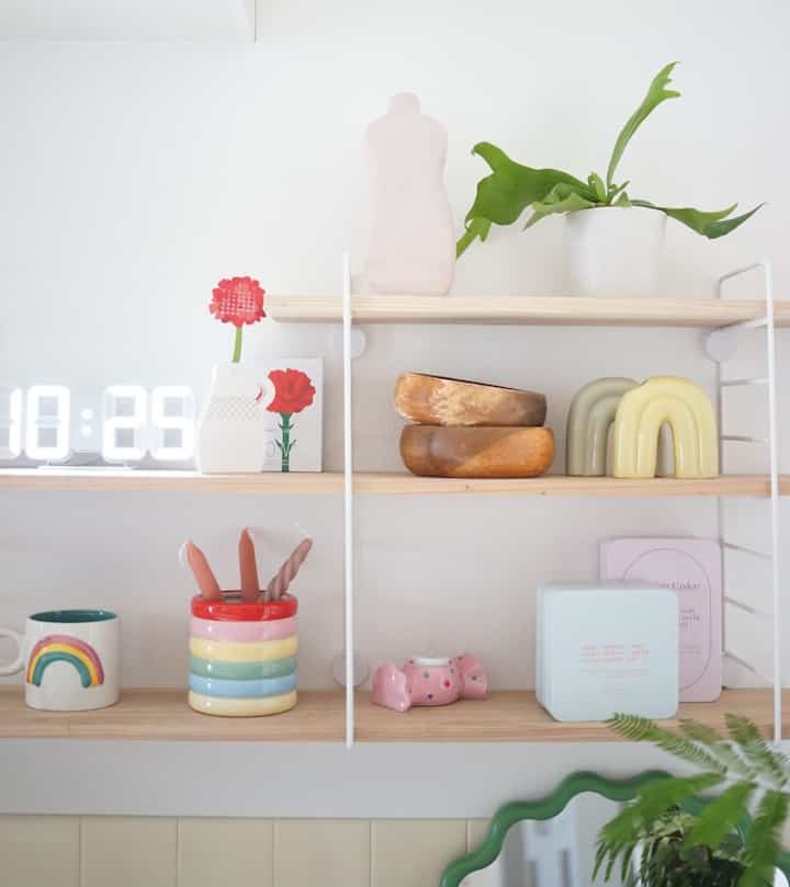 白い壁にナチュラルな木製の棚が設置されたキッチン、カラフルな花瓶と小物がかわいらしく配置された雰囲気のあるインテリア