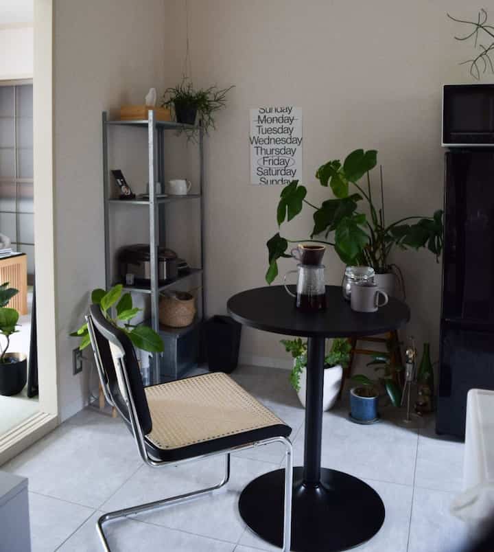 Beige-walled studio with black furniture featuring a cozy home cafe setup, wooden plants, and a small round table contributing to a warm atmosphere