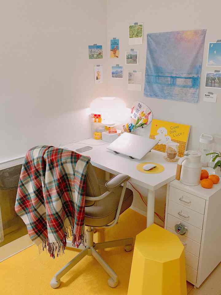 Simple workspace with white walls and yellow flooring featuring a desk, office chair, and laptop in a cozy setup