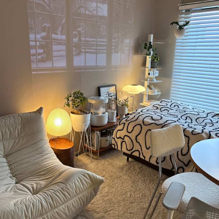 ナチュラルな色調の寝室、ソファベッドとラグ、照明が配置された雰囲気のある空間