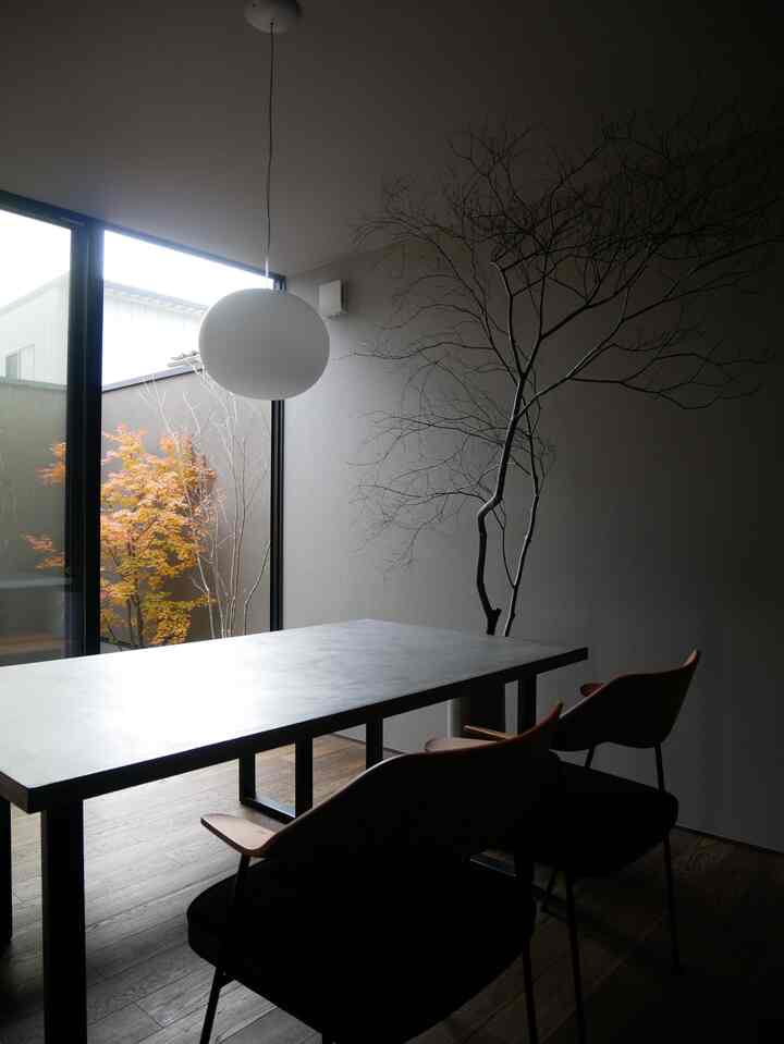 ナチュラルカラーと木目調が調和するモダンな二人用ダイニングルーム、ペンダントライトと窓の外の枝が抜け感を演出する空間