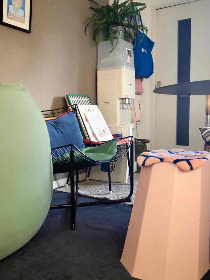 Small, natural-toned room featuring green bean bag, black metal armchair, and pink stool