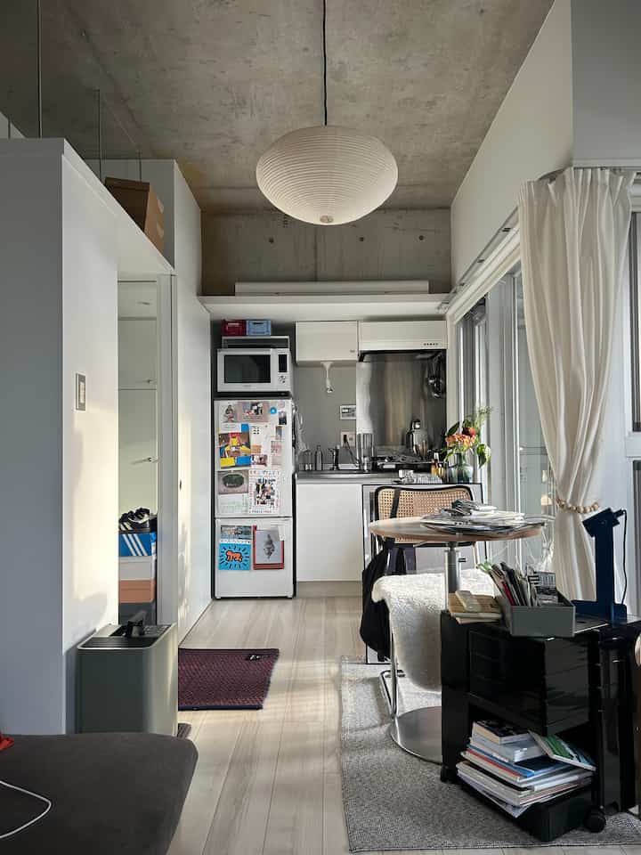 Bright white and wood-tone studio apartment kitchen-living space featuring modern furniture with a slightly cluttered atmosphere