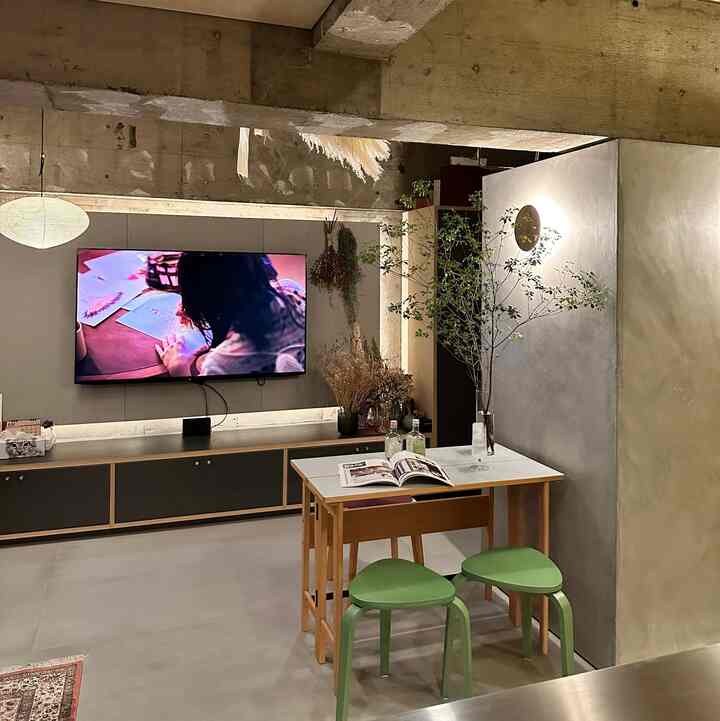 ブラウンのコンクリート天井とホワイトのテーブル、グリーンスツールが配置されたモダンなリビング空間