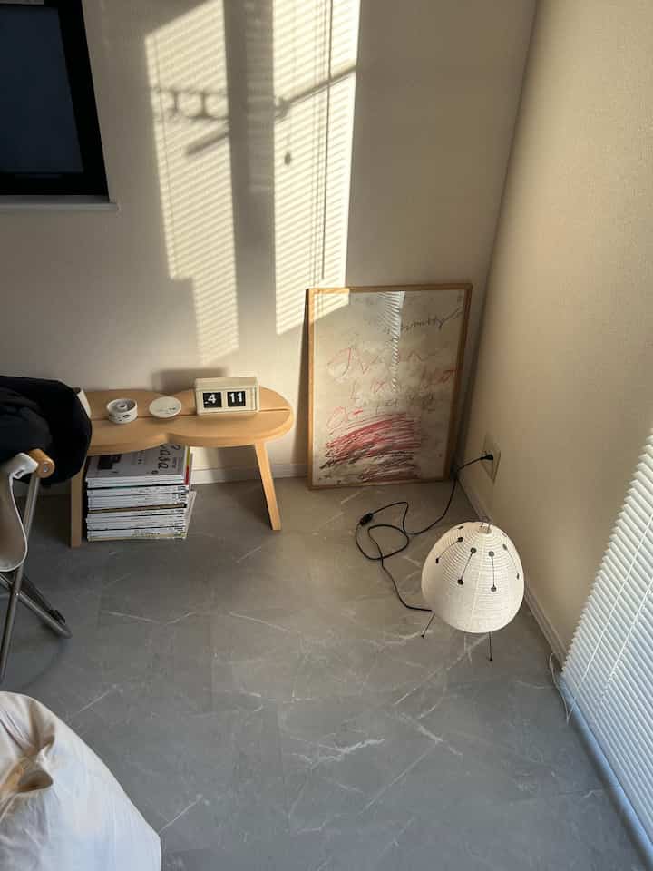 Beige-walled compact room featuring a wooden stool, abstract poster, and floor lamp, with a natural and simple atmosphere
