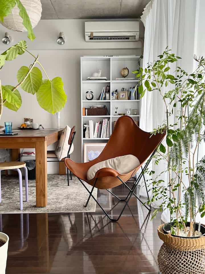 Natural dining room with white walls, brown wooden table, brown leather armchair and prominent green plants