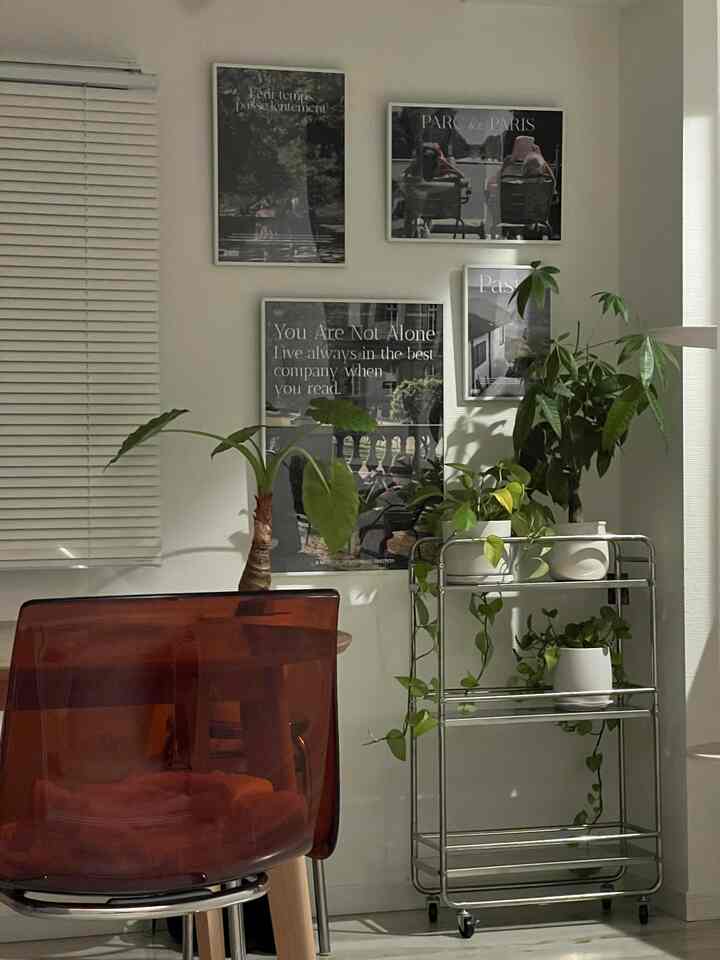 Transparent red chair with silver plant rack and posters on wall, simple home office space with natural elements