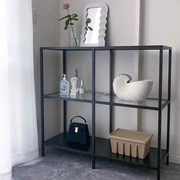 モノトーンの背景に黒のメタル棚と花瓶、彫像などが配置されたシンプルでミニマルなリビングインテリア