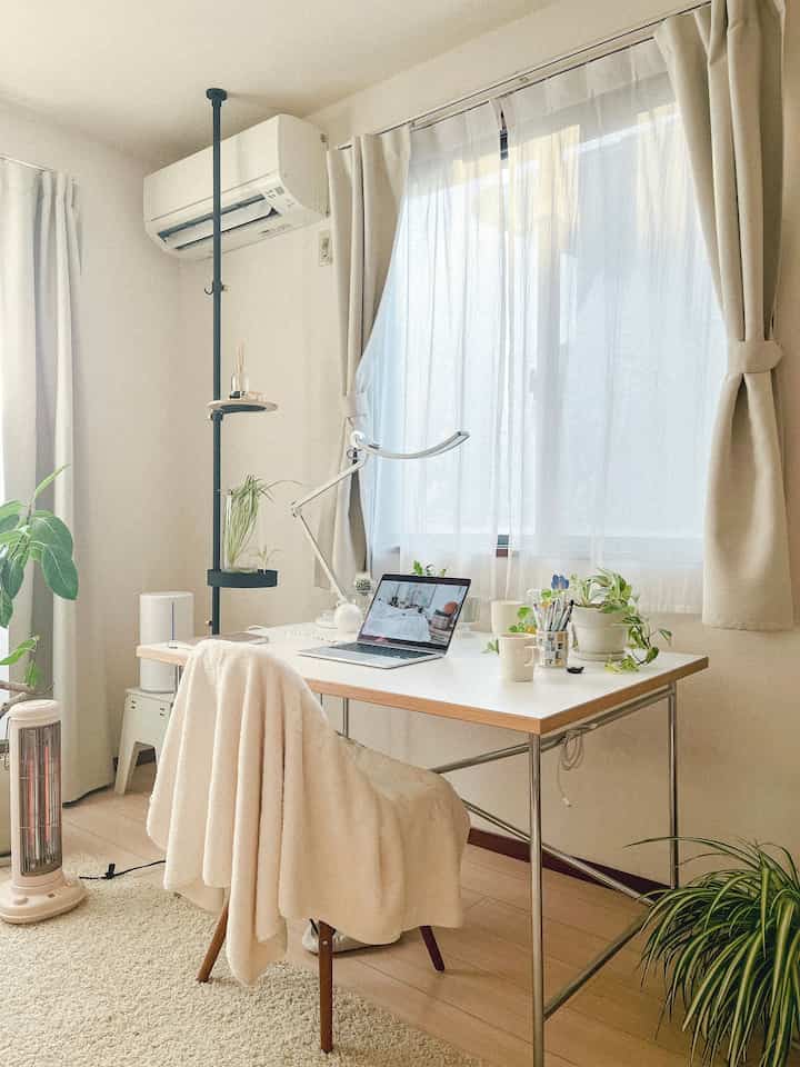 明るいホワイトとベージュのトーンが特徴の一人暮らし用ホームオフィス、植物とブランケットが配置された北欧風の雰囲気のあるインテリア