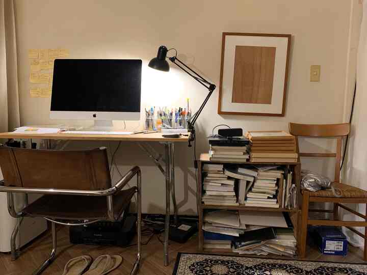 ブラウンとホワイトのトーンのワークスペース、机、椅子、本の山、クランプランプが散らかった印象的な空間