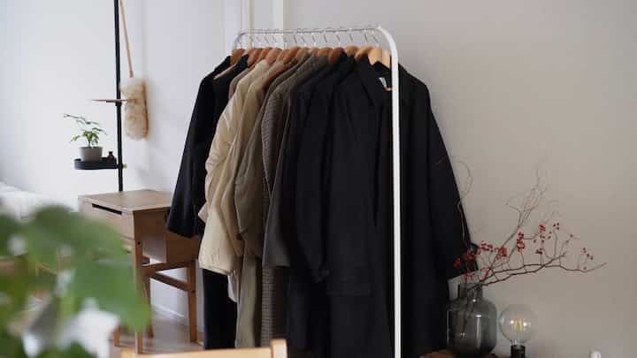 White-walled living room with natural wood tone furniture, featuring a white coat rack neatly holding various winter outerwear, creating a clean interior