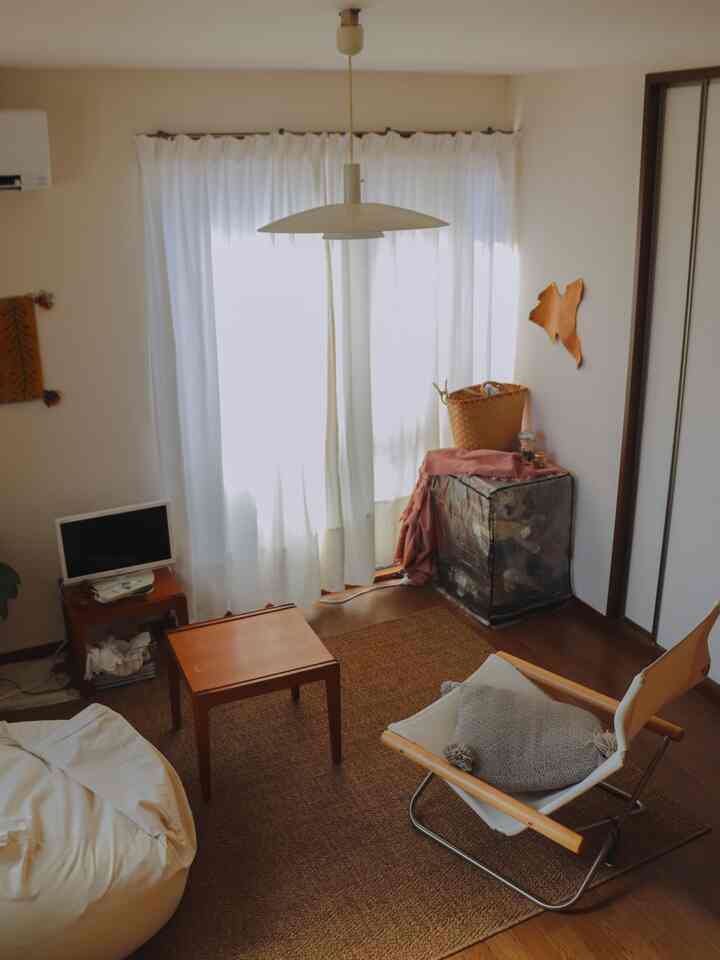 明るい白いカーテンとナチュラルな木製家具が配置されたナチュラルトーンのリビング