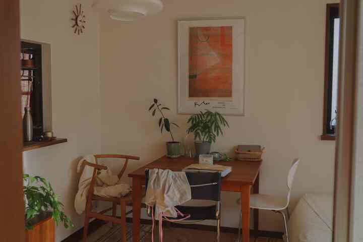 白い壁と茶色のダイニングテーブルがあるナチュラルな北欧風の4人用ダイニング、椅子と植物が配置された雰囲気のある空間