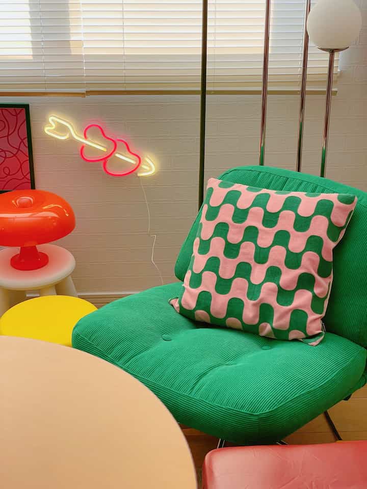 Colorful living room with white wall and blinds background, featuring green rotating armchair and pink-green cushion in retro style