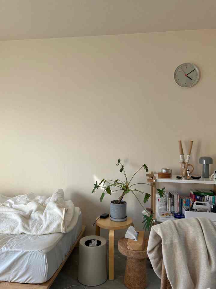 ベージュのトーンが特徴的な寝室、木製スツールと植物が配置された自然で落ち着いた雰囲気のインテリア