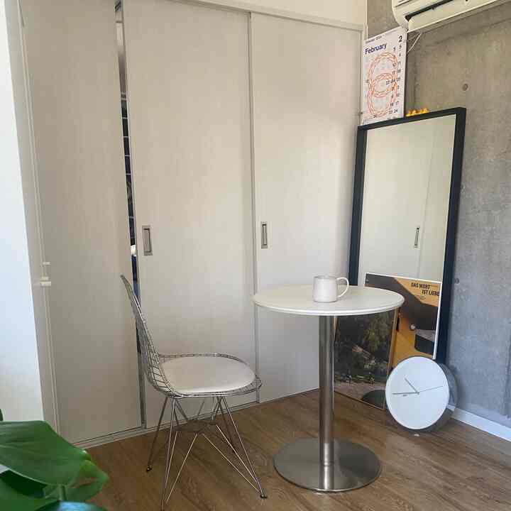 グレーのコンクリート壁と白いスライディングクローゼット、丸テーブルと金属製の椅子が配置されたコンパクトな一人暮らしの部屋