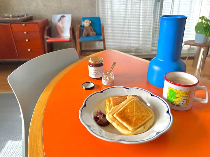 Orange-toned small living room with wooden sideboard, vintage furniture, and a home cafe setup featuring hot sandwiches and coffee