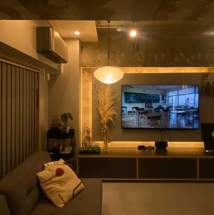 暖かいナチュラルトーンのリビング、グレーのソファとペンダントライト、テレビ台がある雰囲気ある空間