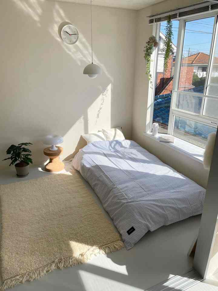 白とベージュのトーンの寝室、窓際にマグニバーグのストライプベッドカバーが配置された暖かな空間