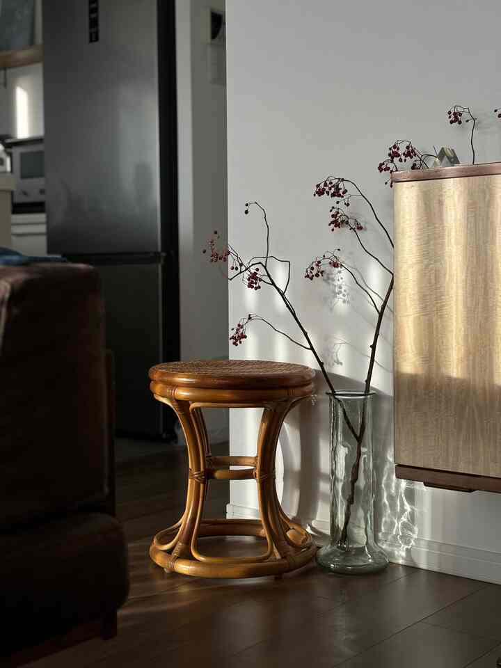 Living room with warm wood tones and white walls, featuring a rattan stool and natural light shadows creating a cozy atmosphere