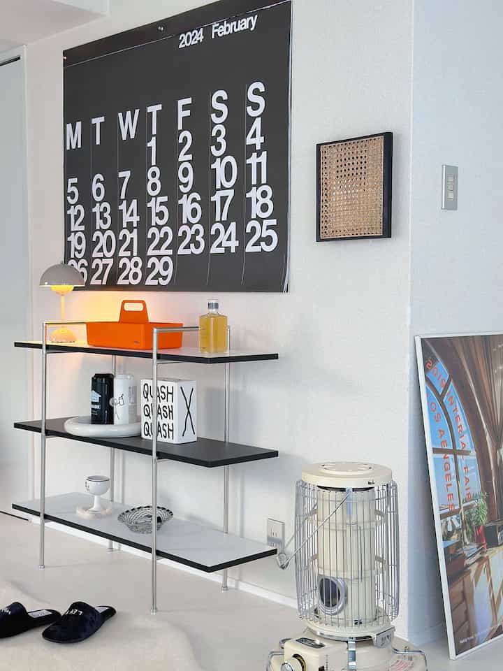 白い背景に黒い棚とオレンジの工具箱が配置されたミニマルで清潔感のあるリビングまたは玄関の空間