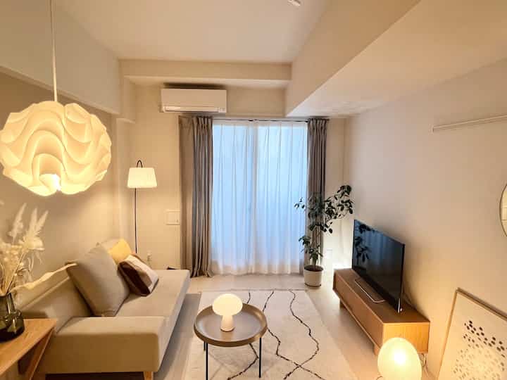 ベージュとナチュラルトーンの一人暮らし用リビング、シンプルなソファと照明が配置された雰囲気のある空間