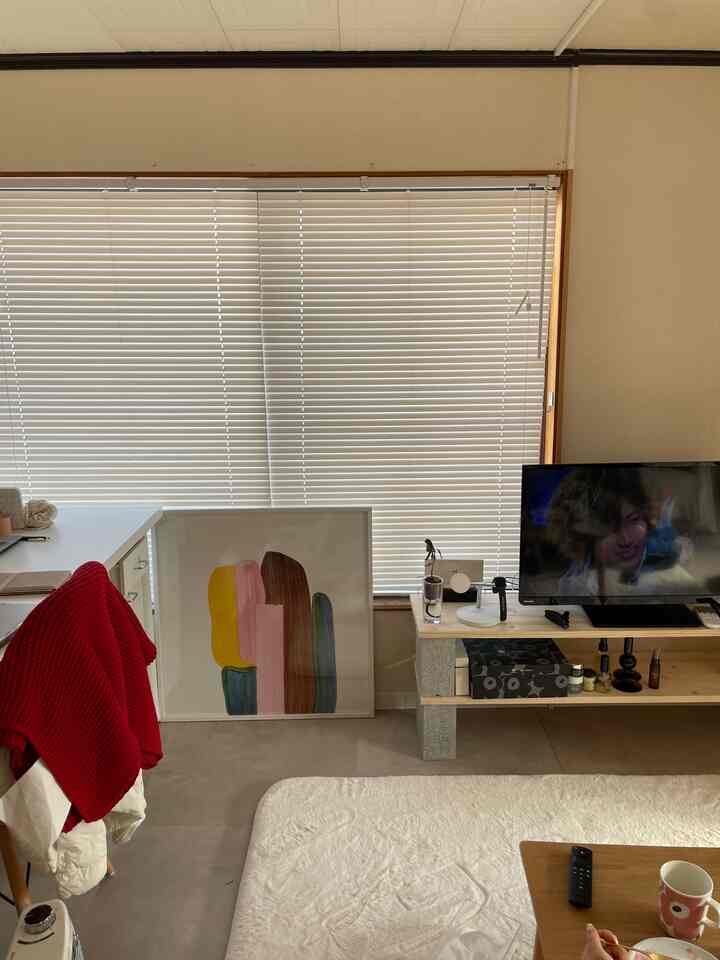 白と茶色のトーンのリビング、大きなブラインド、ポスター、ラグが配置されたシンプルな空間