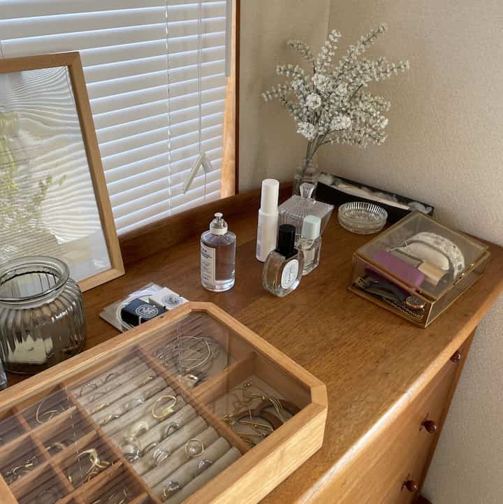 A wood tone chest of drawers with white blinds and organized personal care items, creating a simple elegant corner space