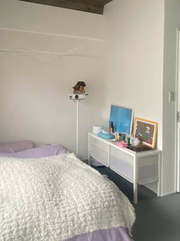 白とライトブラウンの色調の寝室、ベッドとプロジェクター、アロマディフューザーが配置された雰囲気のあるインテリア