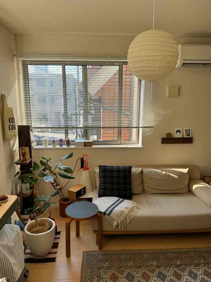 ナチュラルカラーの1LDKリビング、ベージュのソファと木目調のスツール、ペンダントライトが配置された落ち着いた空間