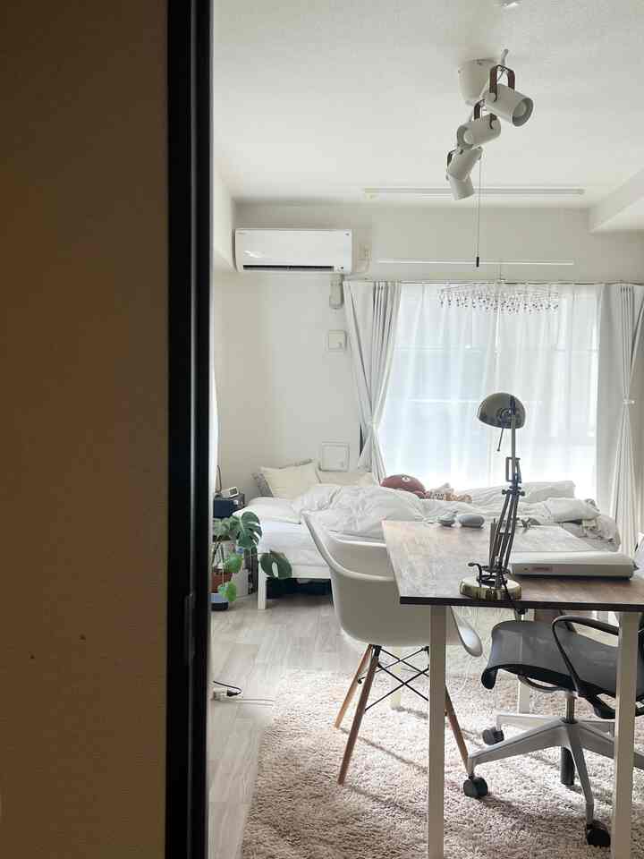 白を基調としたワンルーム寝室、ベッドとデスク、オフィスチェアが配置された清潔で落ち着いた雰囲気のインテリア