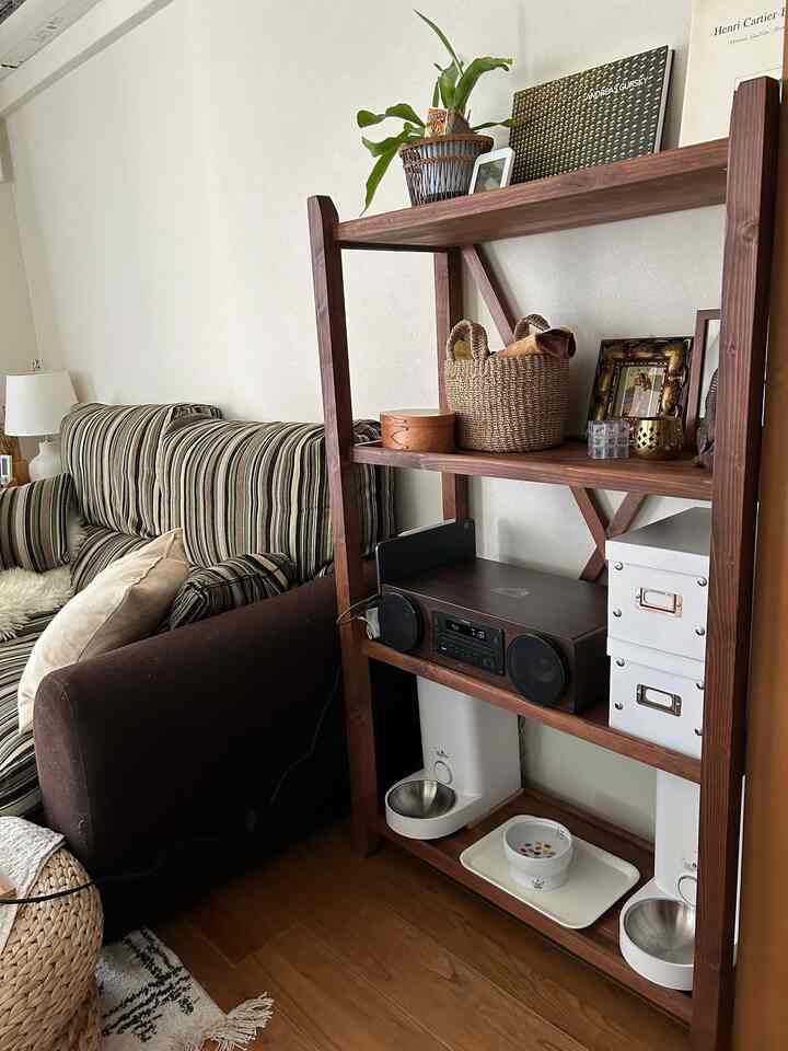 Brown wood tone living room featuring striped sofa and open shelf with automated cat feeder, natural and simple interior