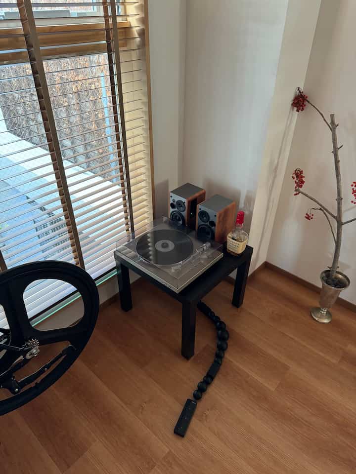 木目調の床と黒いテーブルの上にデノンのターンテーブルとスピーカーが配置されたミニマルなリビングコーナー