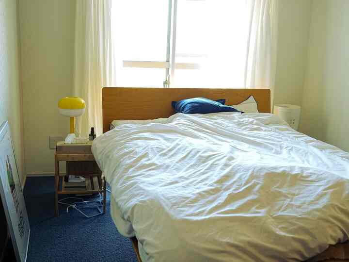 白と木目調が調和する寝室、ネイビークッションと黄色のランプがアクセントの明るく居心地の良いインテリア