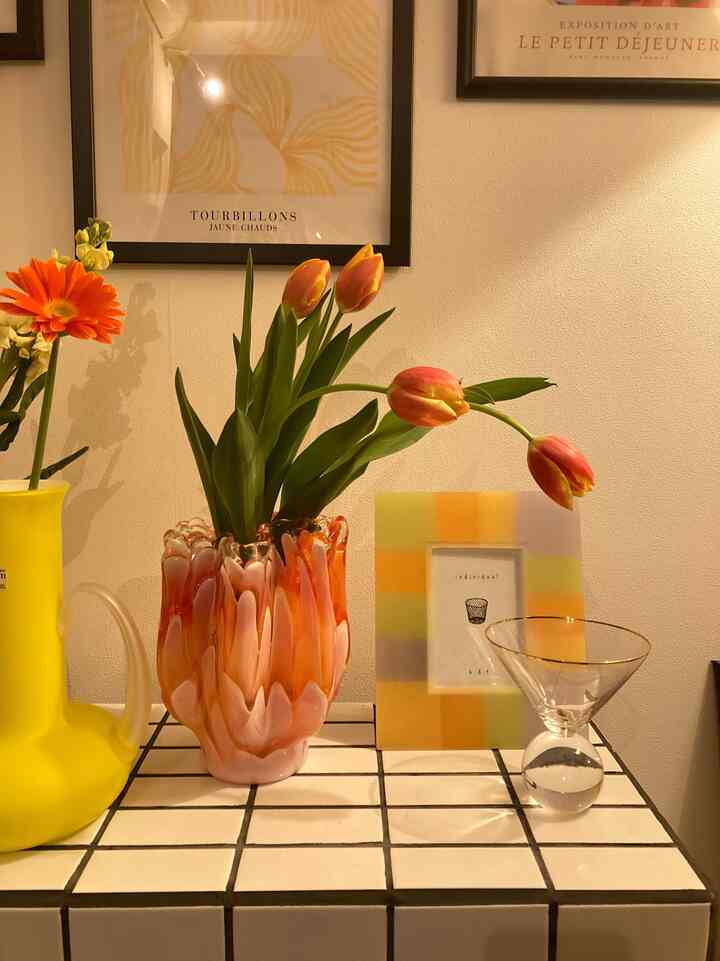 黄色とオレンジのトーンがあるリビングの一角、ヴィンテージの花瓶にチューリップとアートポスターが配置された雰囲気のあるインテリア