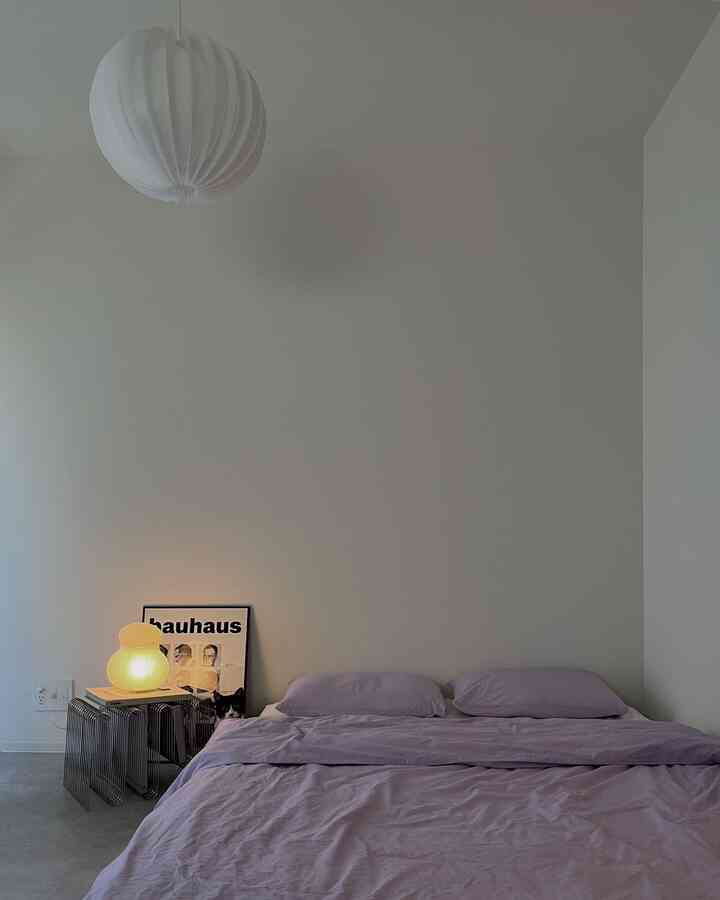 白い壁と天井の寝室、パープルの寝具とサイドテーブルに温かい灯りのある雰囲気のあるインテリア