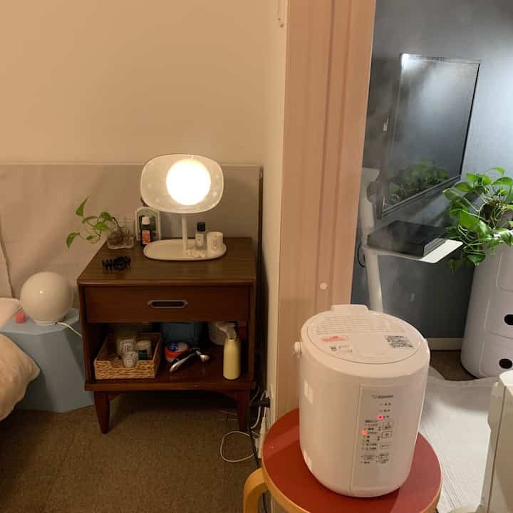 Cozy studio apartment bedroom-living space in soft white and brown tones featuring humidifier, stool, and large mirror