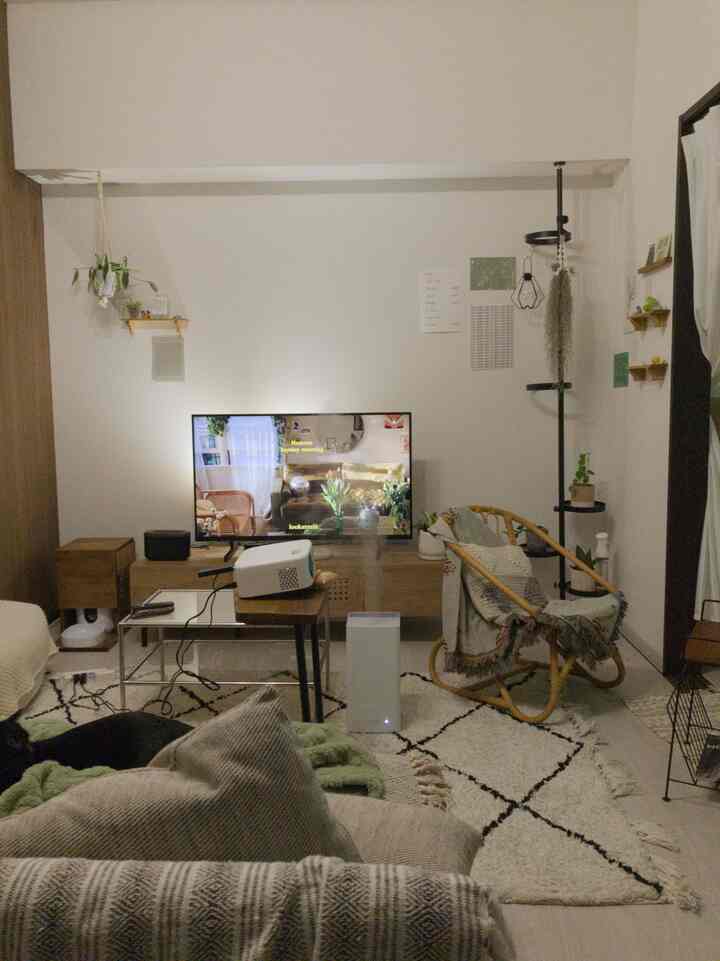 Bright white-walled compact living room featuring wood-tone furniture, a projector, and TV creating a cozy home cinema atmosphere