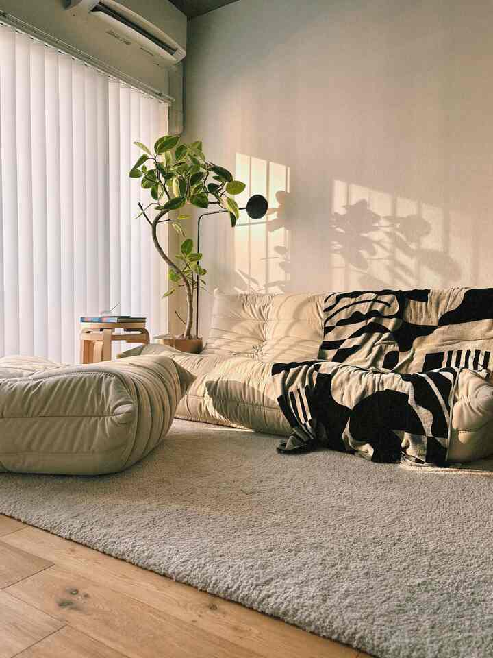 ベージュと木目調が調和したリビング、ベージュのソファとオットマン、大きなラグが配されたナチュラルモダンな印象の空間