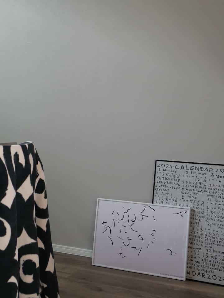 明るい白い壁と木製の床、床に置かれた白黒のパターンポスターがあるシンプルな空間