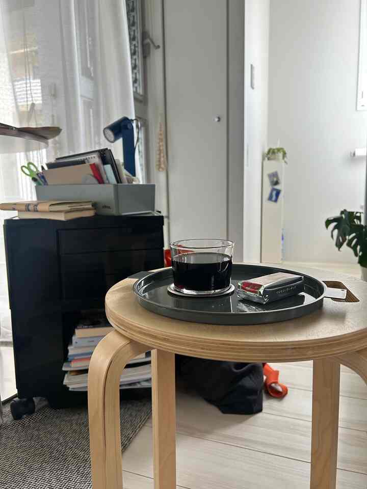 Studio apartment with white walls and floor featuring a natural wood tone stool topped with a gray tray holding a glass cup of coffee