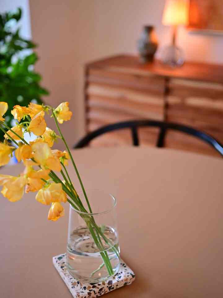 A warm beige-toned round dining room table featuring a glass vase with yellow flowers creating a natural atmosphere